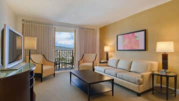 A hotel room with a sofa, two armchairs, a coffee table, a TV, and a balcony with curtains.