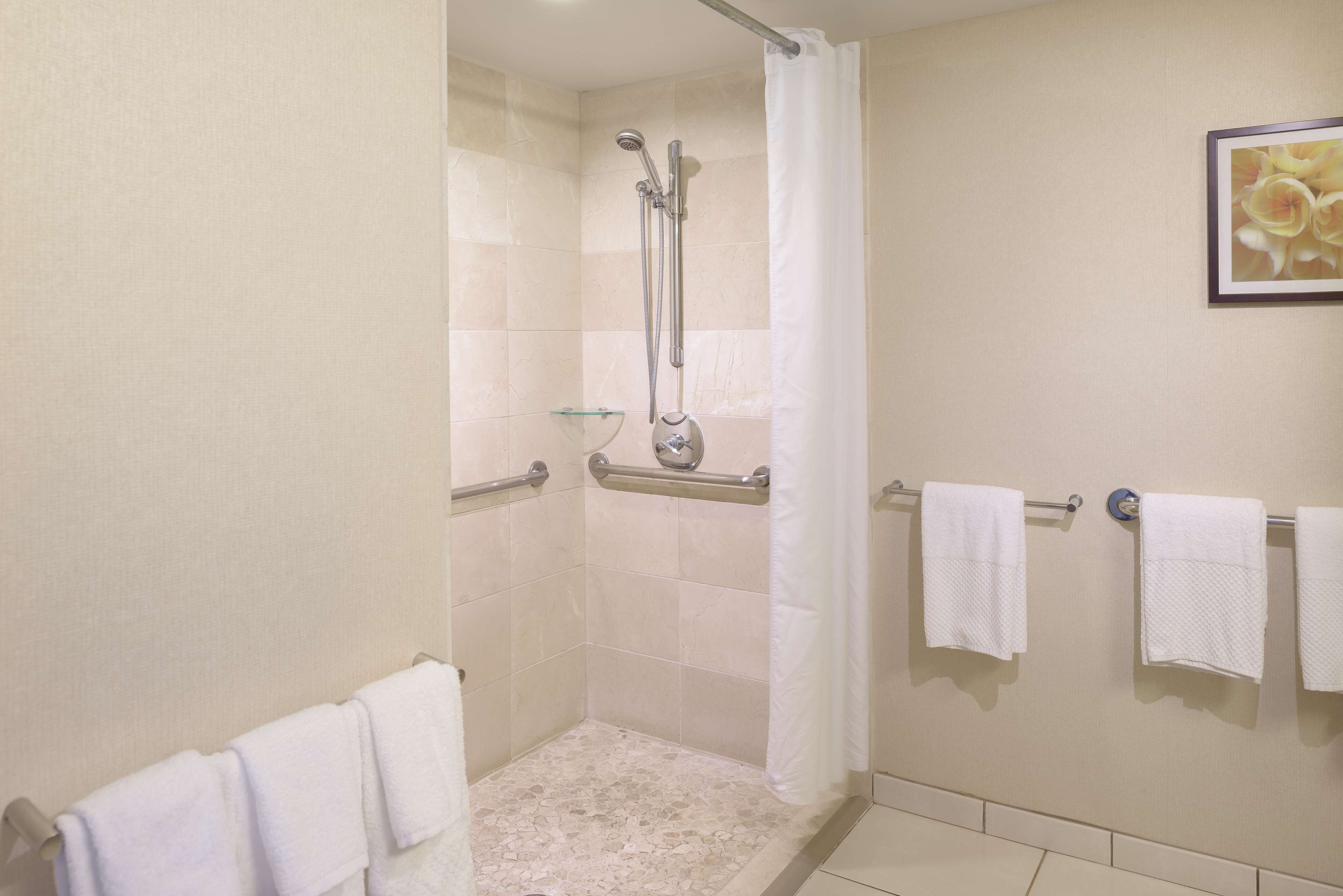 A shower area with a glass shelf, a handrail, and a towel rack with three towels.