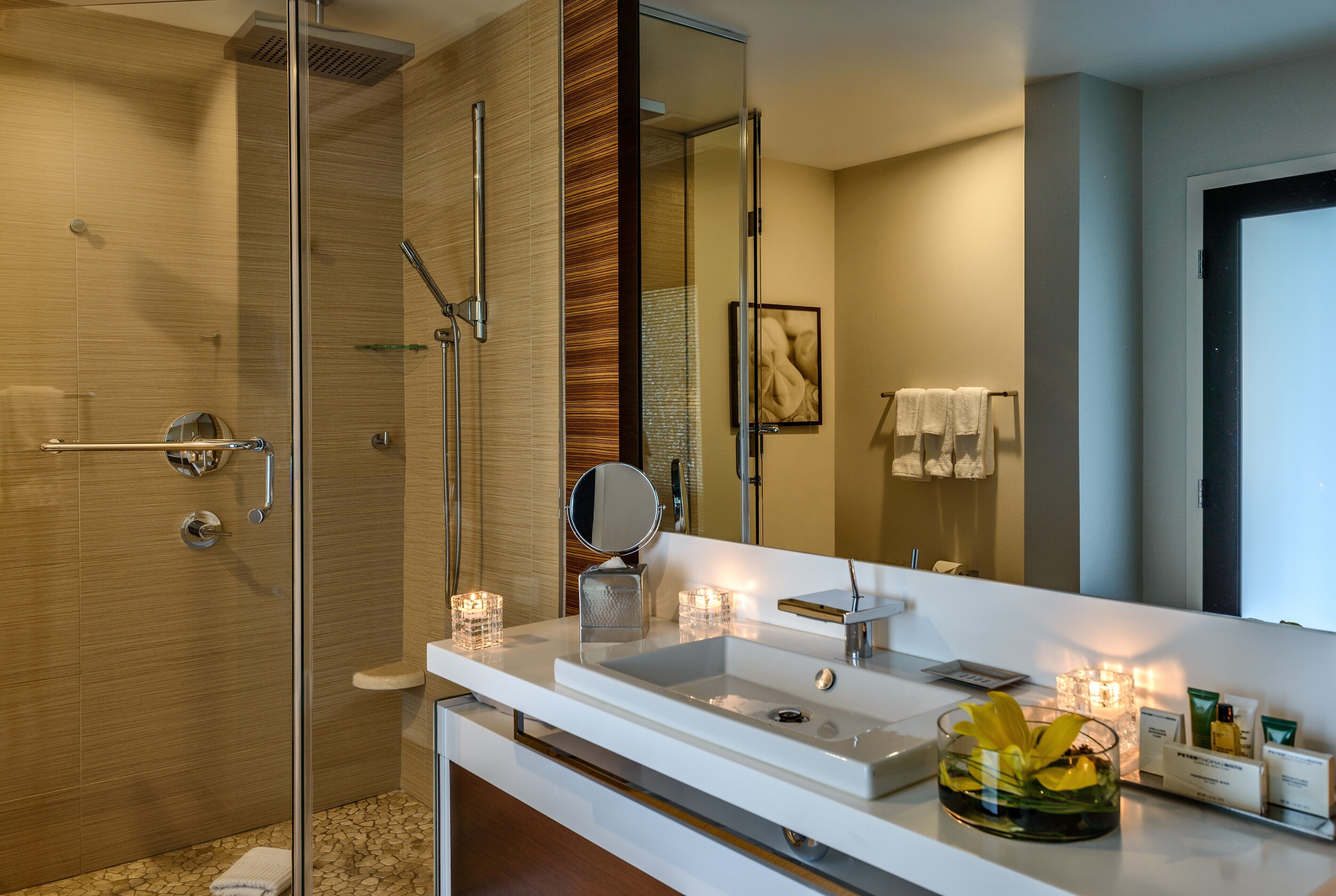 A modern bathroom with a glass shower enclosure, a white sink with a mirror, and a glass vase with flowers.