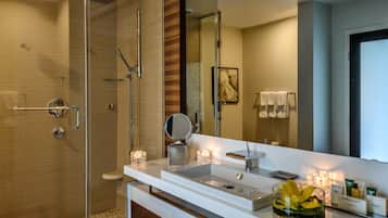 A modern bathroom with a glass shower enclosure, a white sink with a mirror, and a glass vase with flowers.