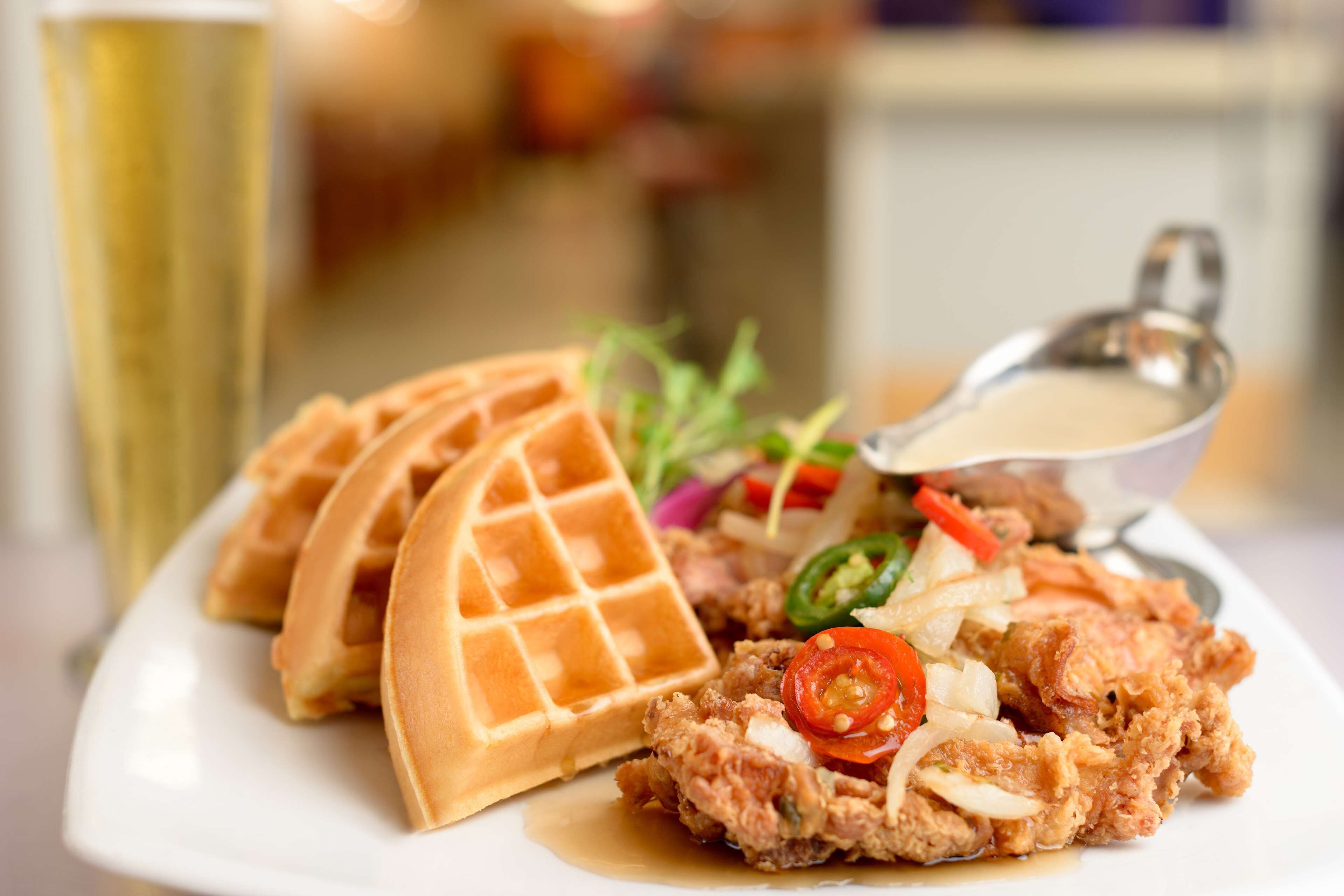 A plate with waffles, fried chicken, and a small bowl of sauce.