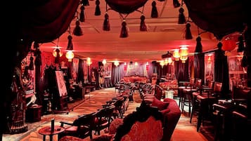 A dimly lit room with red curtains, hanging lanterns, and a variety of seating arrangements including sofas and chairs.