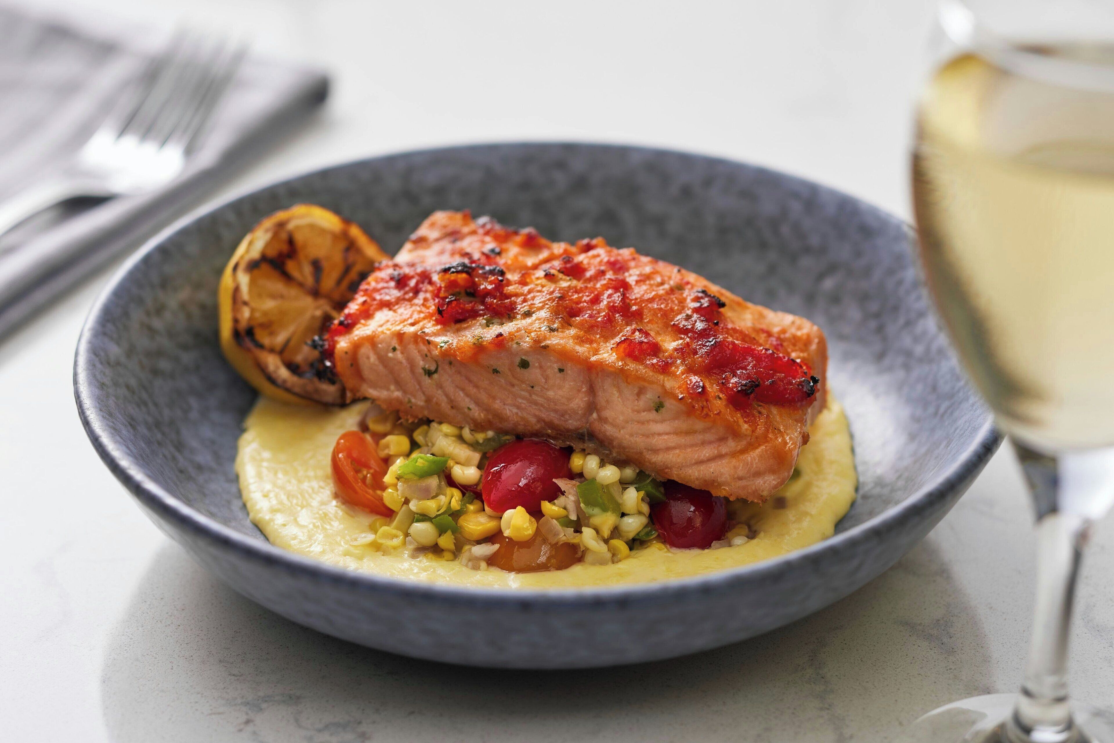 Une assiette de saumon accompagnée d’une portion de maïs et de tomates cerises.