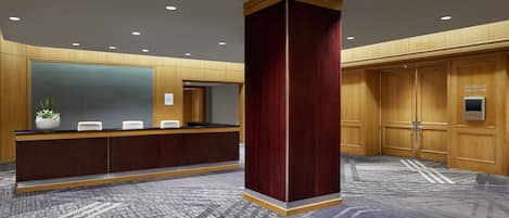 Un espace d’accueil comprenant un comptoir de réception, une grande colonne en bois et un panneau indiquant l’entrée de la salle de bal Arlington.