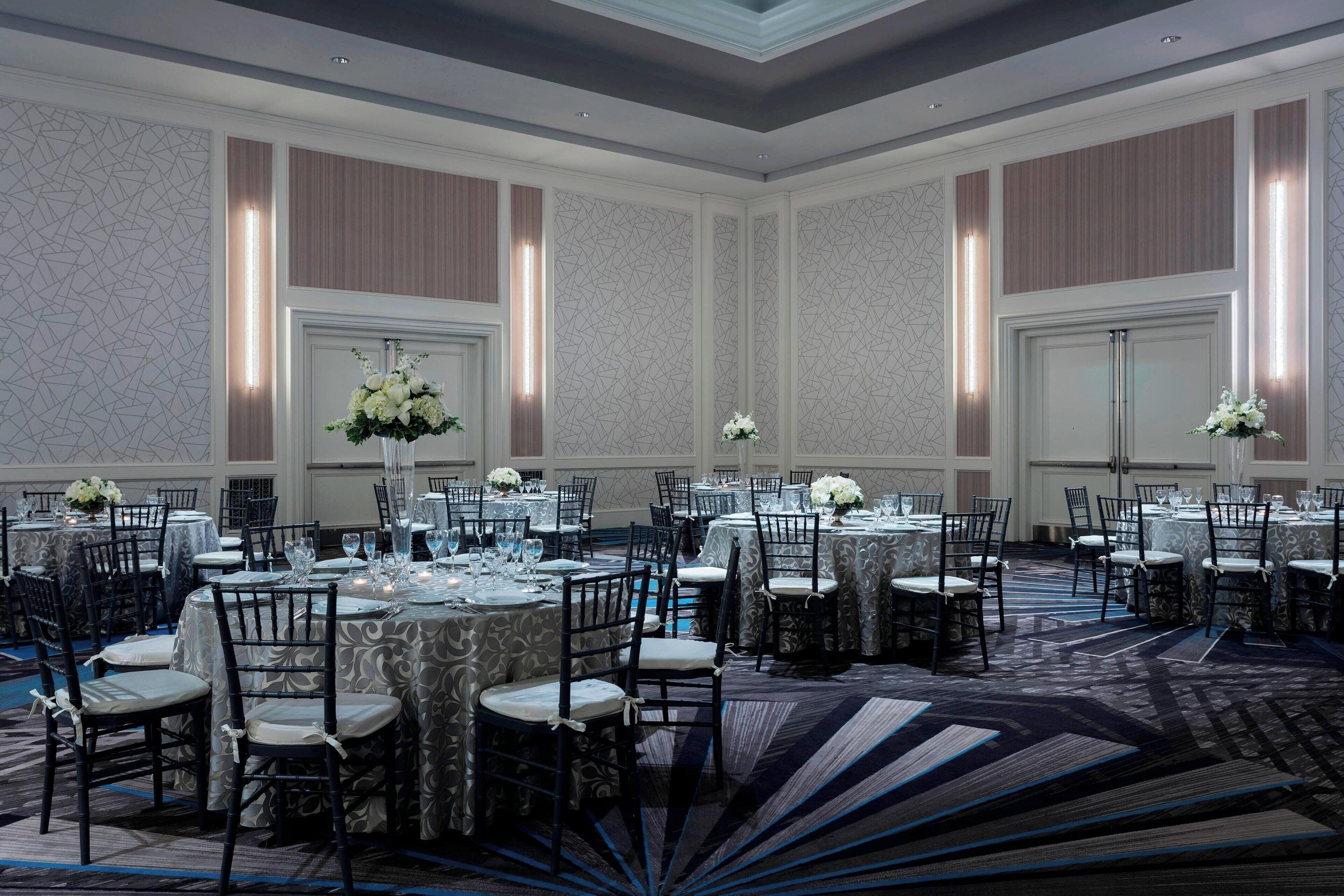Un salón de banquetes con mesas redondas, sillas y centros de mesa florales.
