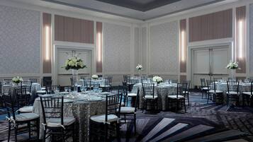 Un salón de banquetes con mesas redondas, sillas y centros de mesa florales.