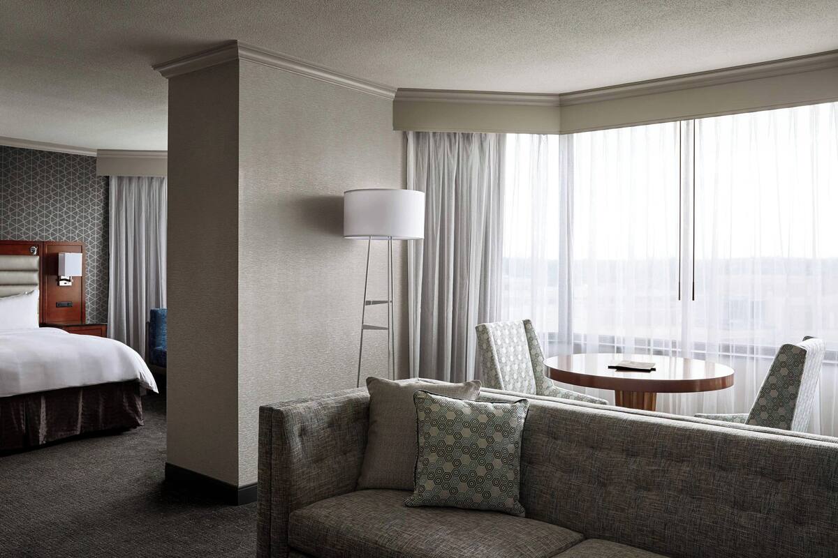 A hotel room with a bed, a sofa, a table, and a lamp.