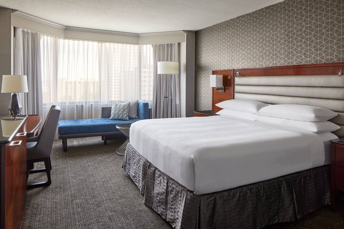 A hotel room with a large bed, a desk, a chair, a sofa, and a window with curtains.