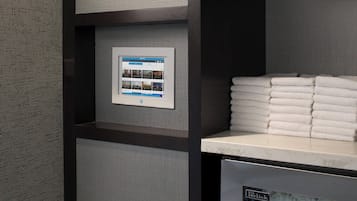 A bathroom with a towel dispenser, a control panel, and neatly stacked towels.