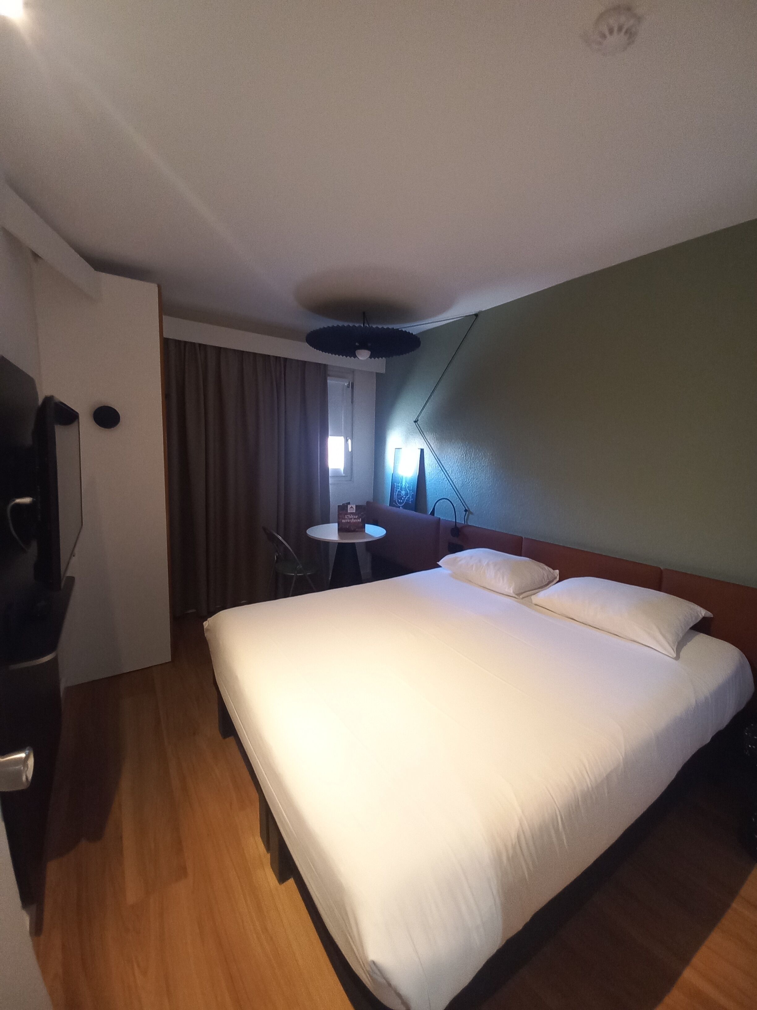 Une chambre d’hôtel avec un lit, un bureau, une chaise, une petite table et une fenêtre avec des rideaux.