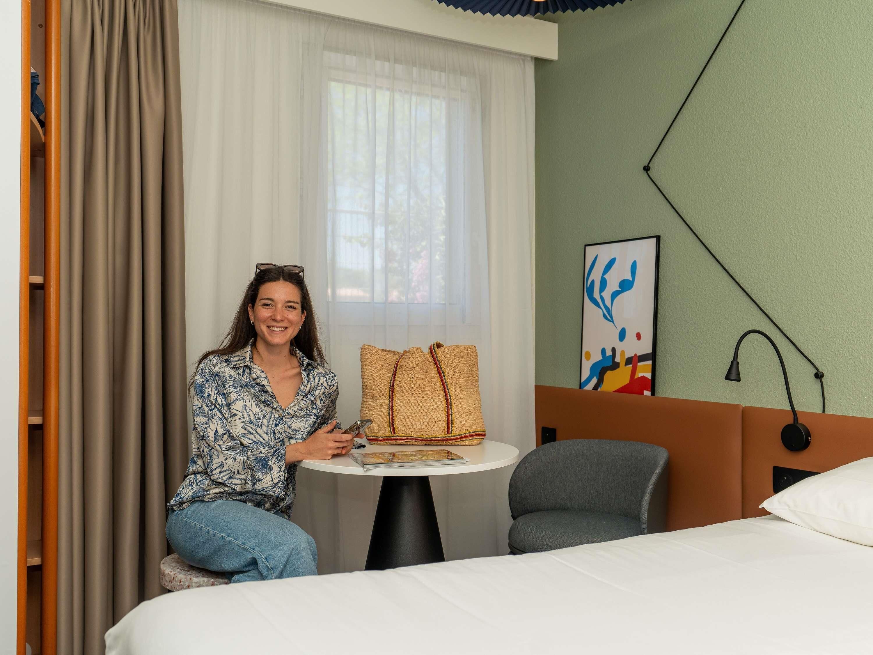 Ein Hotelzimmer mit einem Bett, einem runden Tisch, einem Sessel, einer Couch, einer Lampe und einem Gemälde an der Wand.