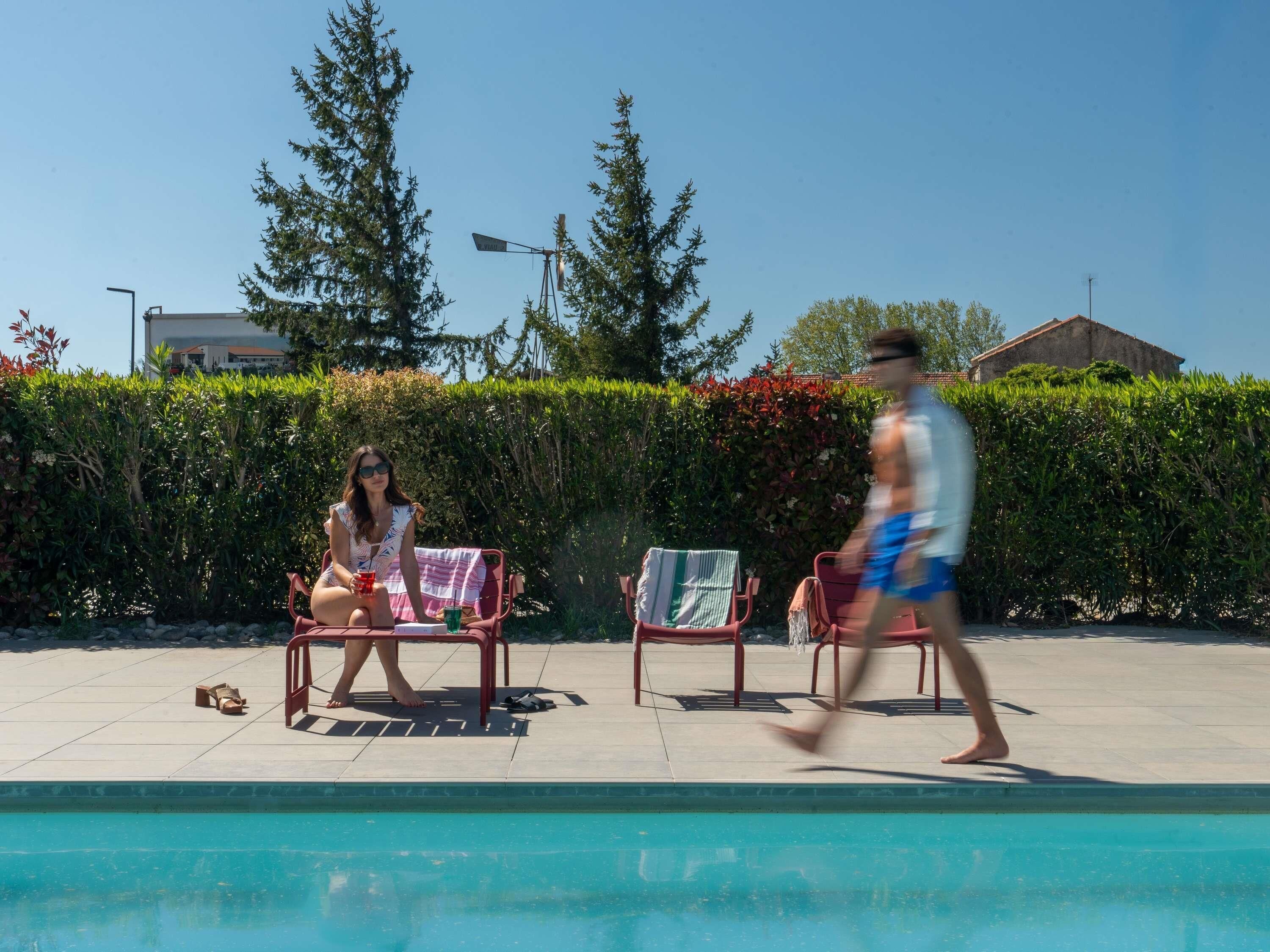 En swimmingpool med solstolar och en häck i bakgrunden.