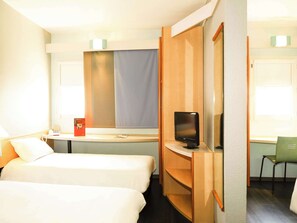 Two single beds with white linens, a desk with flat-screen TV, and a green chair.