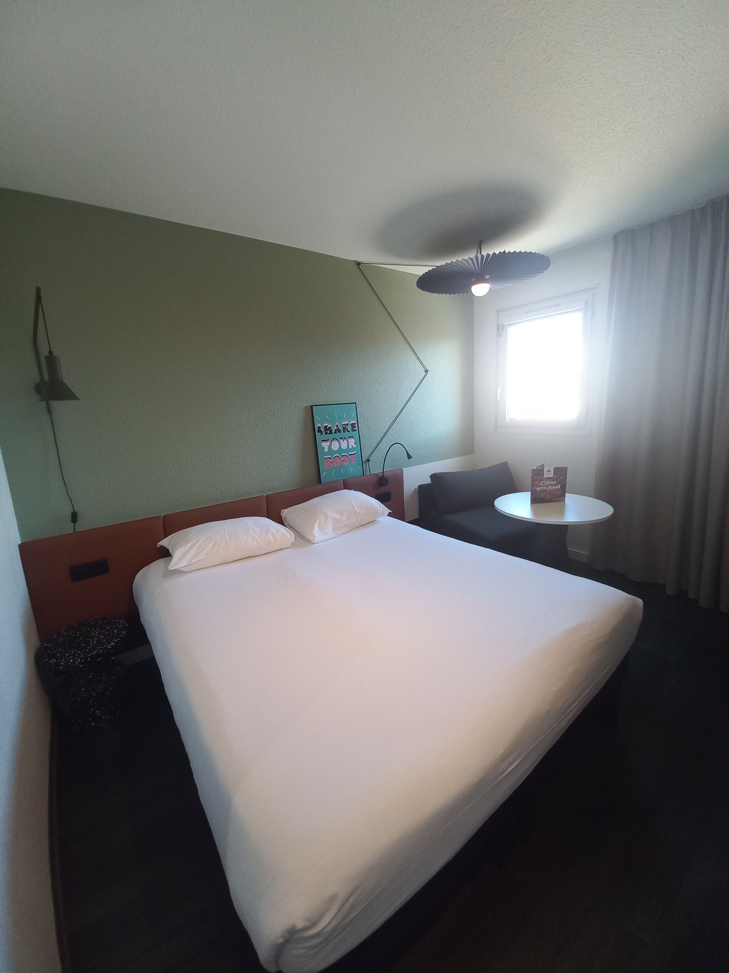 A hotel room with a large bed, a desk, a chair, a lamp, and a window with curtains.