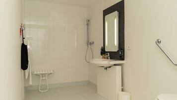 A bathroom with a white sink, a mirror with a textured frame, a handheld showerhead, a toilet, and a towel rack with a black bag.