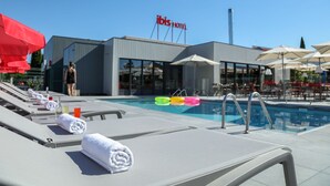 Zona de piscina de hotel con sillas de descanso, sombrillas y cielo despejado.