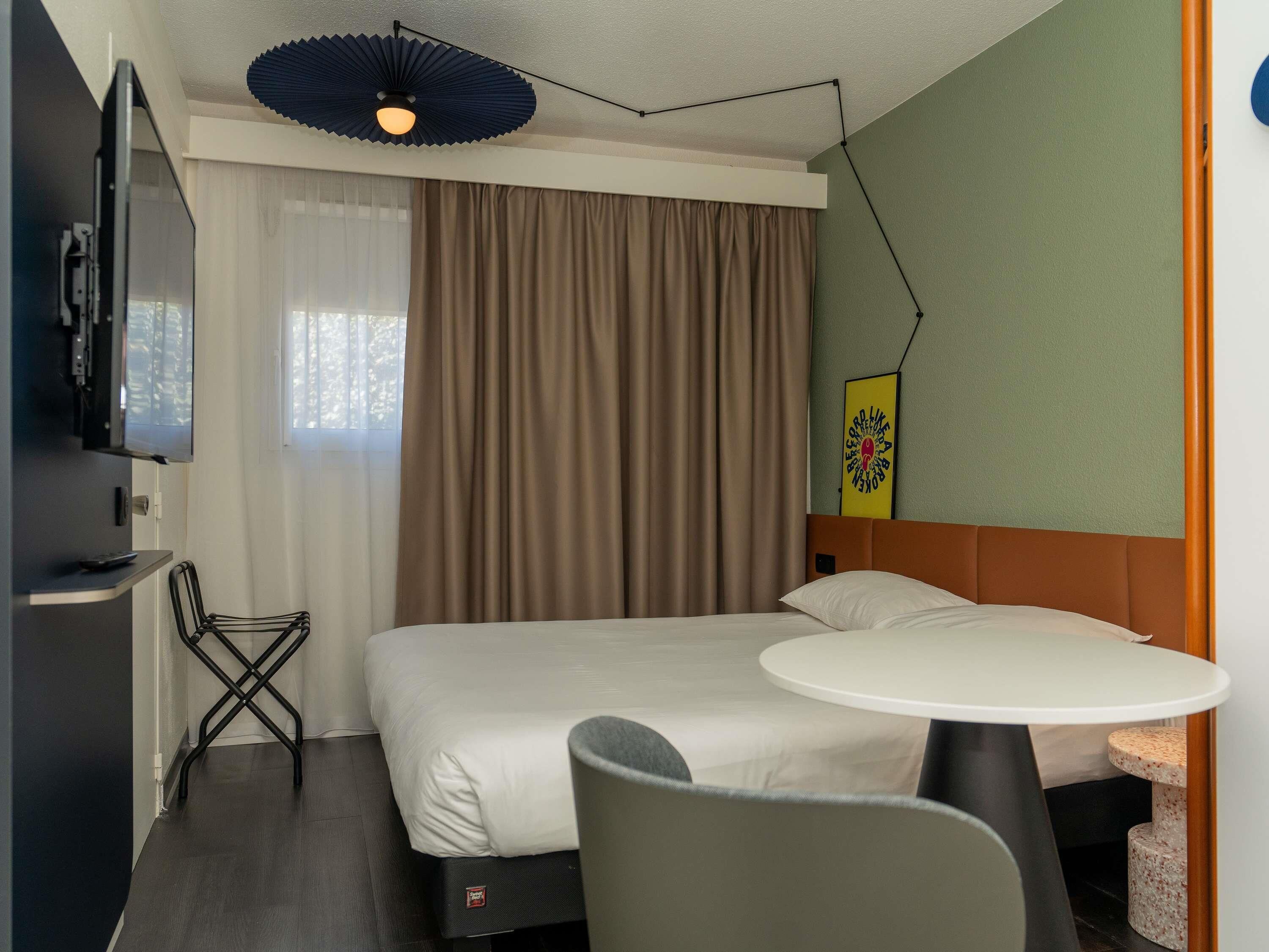 A hotel room with a bed, a desk, a chair, a round table, and a ceiling light fixture.