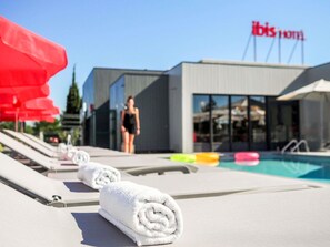 A hotel pool area with lounge chairs, a swimming pool, and a building with 'ibis hotel' signage. - ibis Orange Centre Echangeur A7 A9 (Orange)
