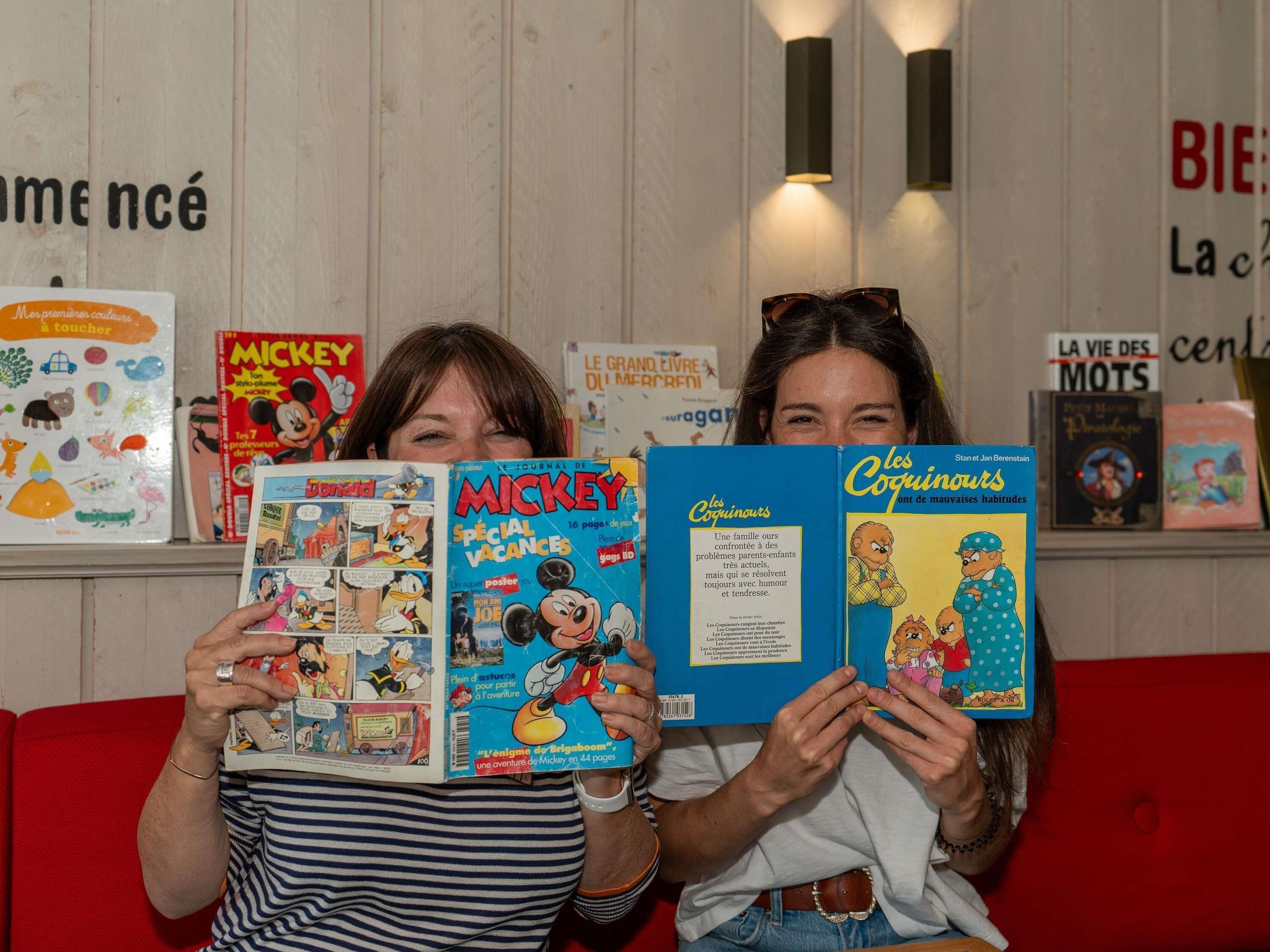 Deux personnes tenant des livres, l’un intitulé « MICKEY SPECIAL VACANCES » et l’autre « Les Coguinguots ».
