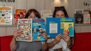 Deux personnes tenant des livres, l’un intitulé « MICKEY SPECIAL VACANCES » et l’autre « Les Coguinguots ».