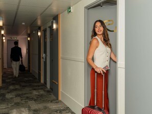 A hotel corridor with doors, a person walking, and a suitcase.