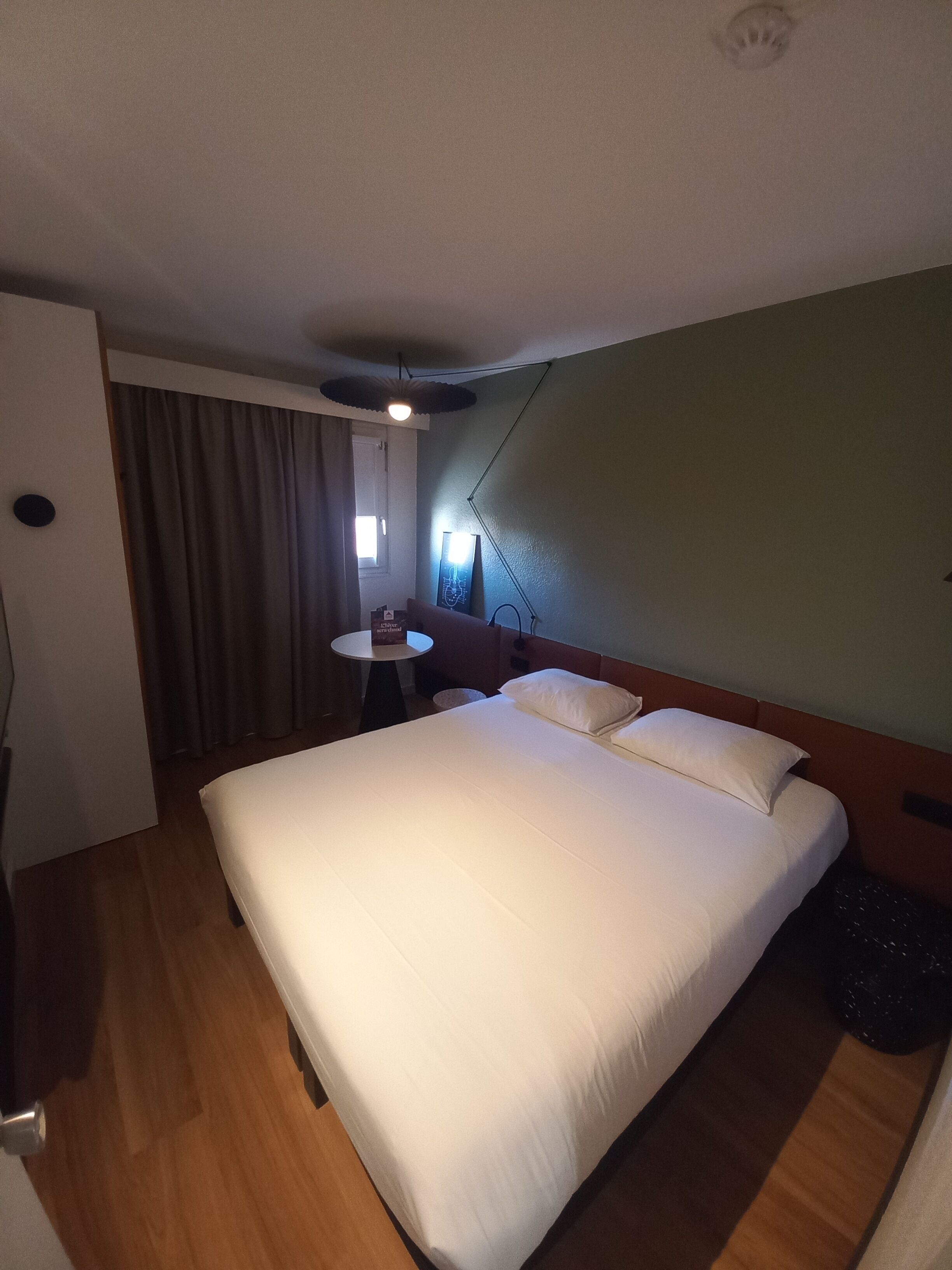 Una camera d'albergo con un letto grande, un tavolino rotondo e una finestra con tende.