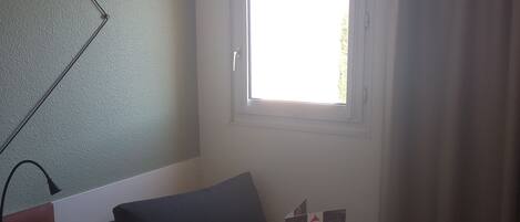 A hotel room with a bed, a round table with a book, a window with curtains, and a ceiling fan.