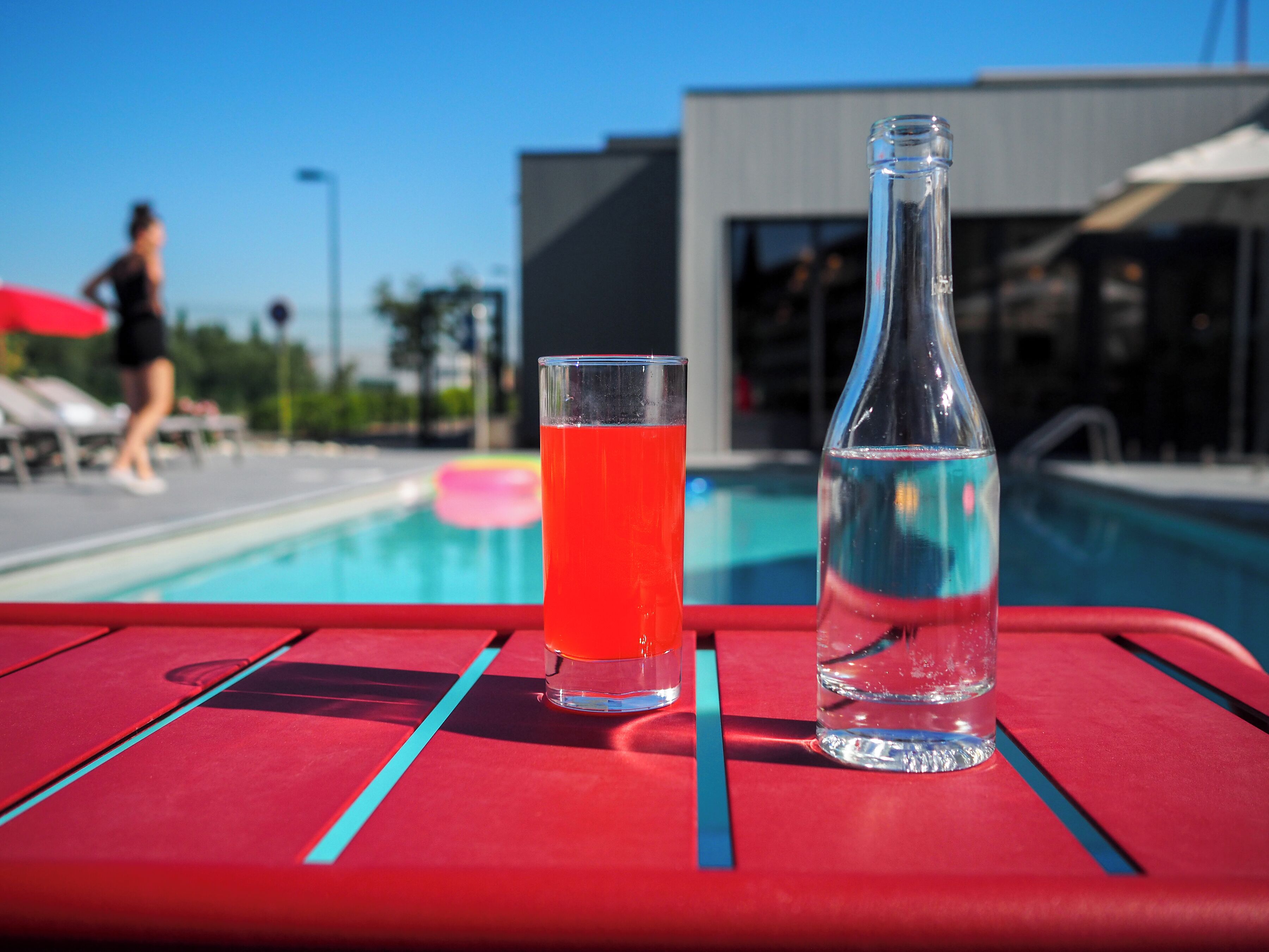 Mesa à beira da piscina, com um copo de líquido vermelho e uma garrafa transparente.