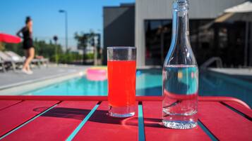Mesa à beira da piscina, com um copo de líquido vermelho e uma garrafa transparente.