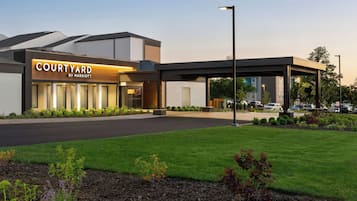 L’entrée d’un hôtel Courtyard by Marriott moderne, avec un passage couvert, un jardin aménagé et un parking.