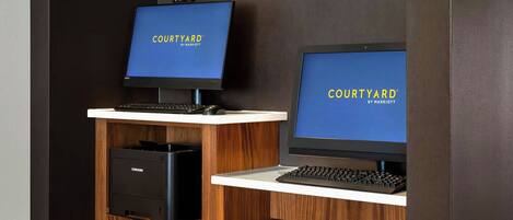Una zona de recepción con dos estaciones de ordenador, un letrero que dice 'Quick Print' y un letrero de 'Courtyard by Marriott' en los monitores.