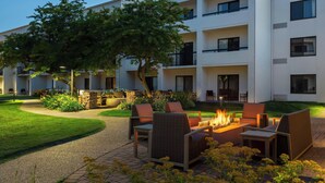 Un patio de hotel moderno con mobiliario exterior, una fogata y un césped bien cuidado.