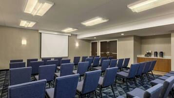 A conference room with rows of chairs, a projector screen, and a kitchenette area.