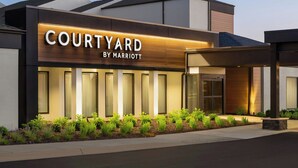 Entrada de un moderno hotel Courtyard by Marriott con fachada bien iluminada, ventanas amplias y un área de jardín ajardinado.