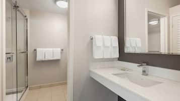 Een moderne badkamer met een glazen douchecabine, een witte wastafel en een grote spiegel.