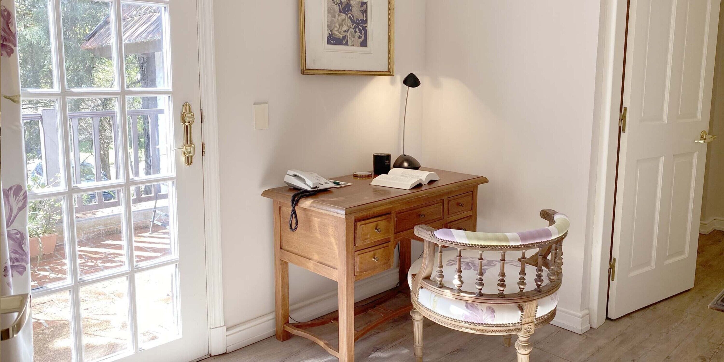 A wooden desk with a telephone, a lamp, and a chair with a floral pattern.