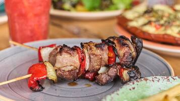 Ein Teller mit Spießen, Fleisch und Gemüse, ein Glas rotes Getränk, eine Schüssel Pommes und ein Salat.