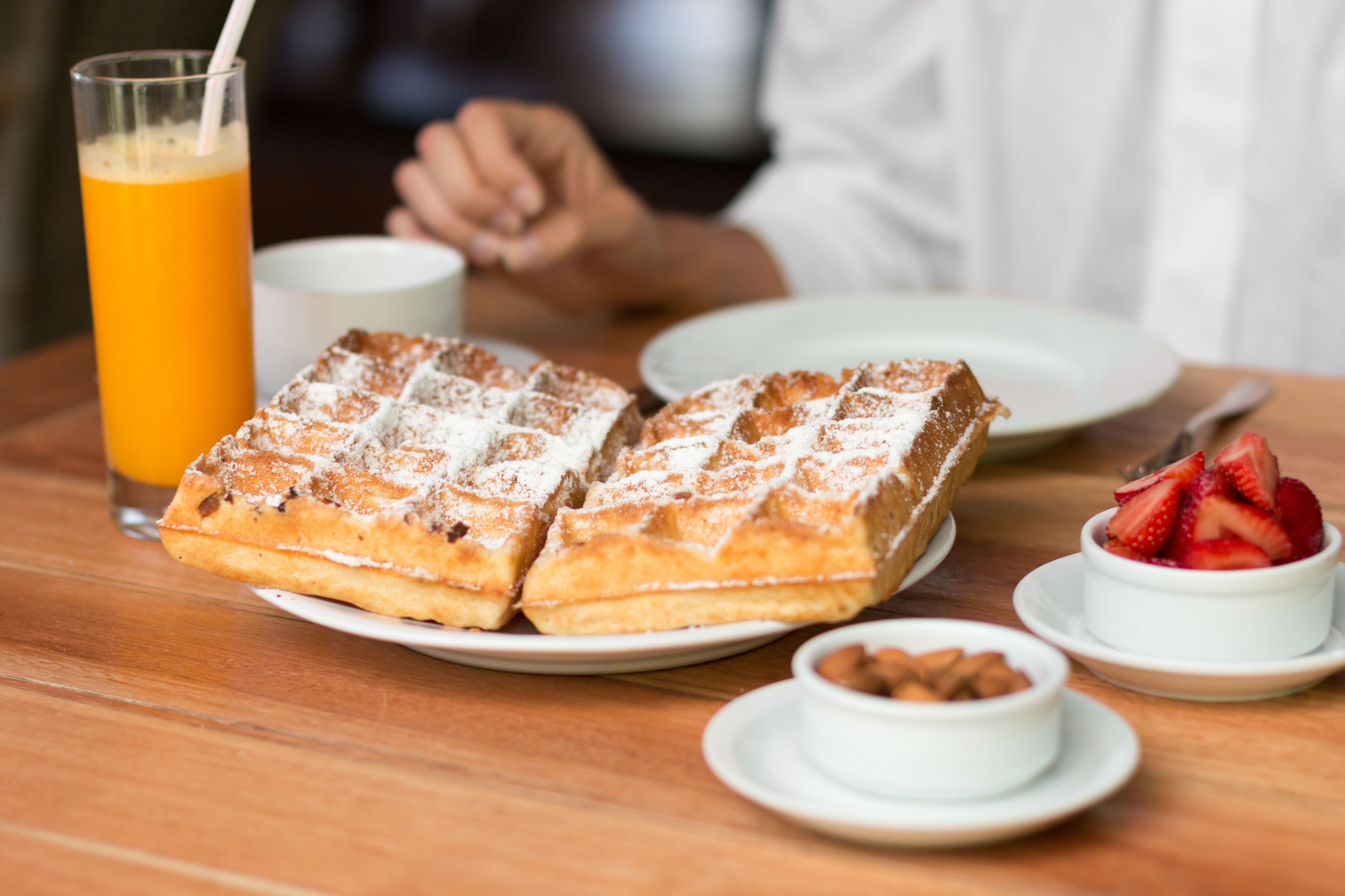 A breakfast setting with waffles, a glass of orange juice, a cup of coffee, and a bowl of strawberries and almonds.