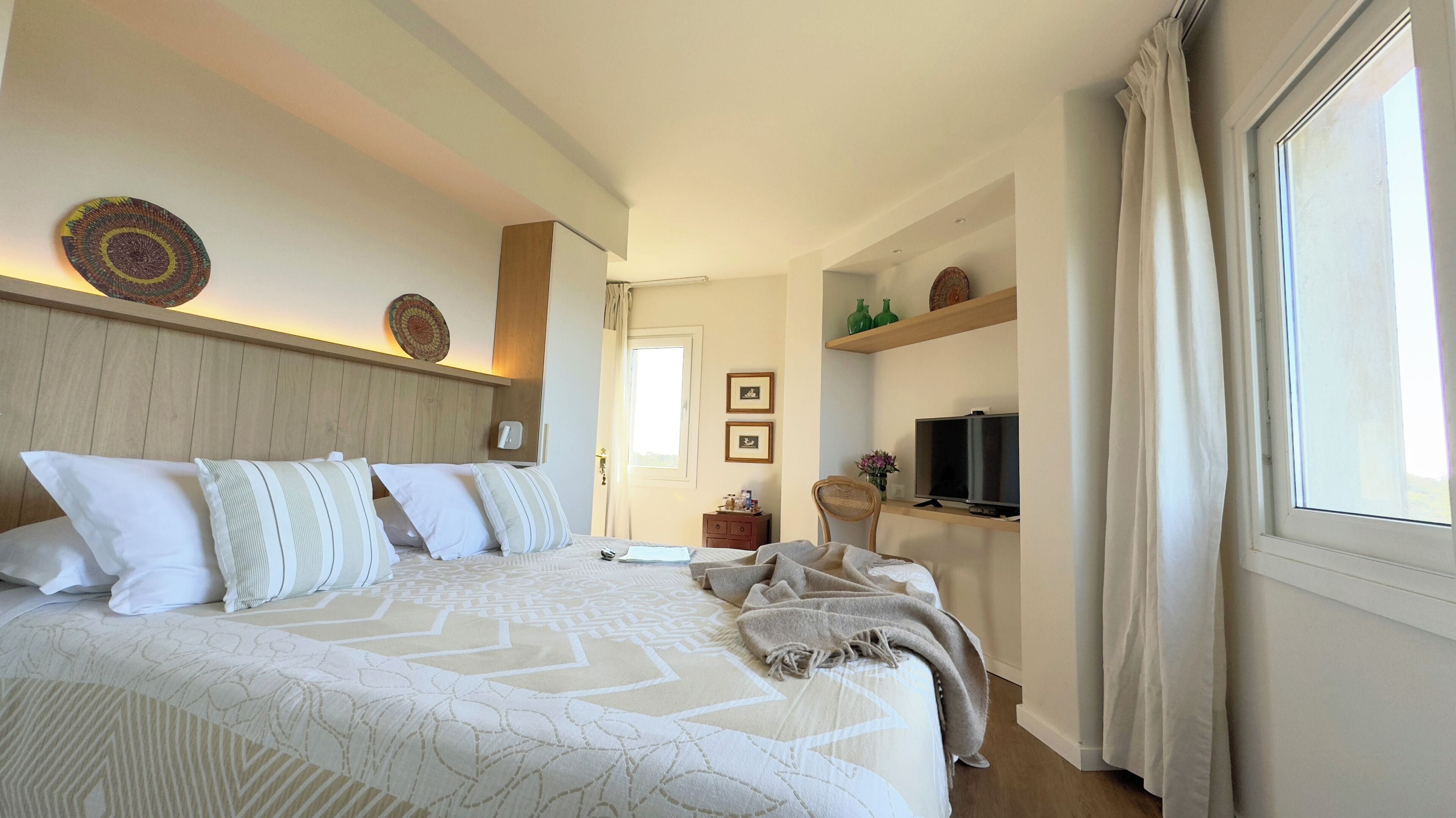 Ein Hotelzimmer mit einem großen Bett, einem Fernseher, einer Ablage mit Dekoration und einem Fenster mit Vorhängen.