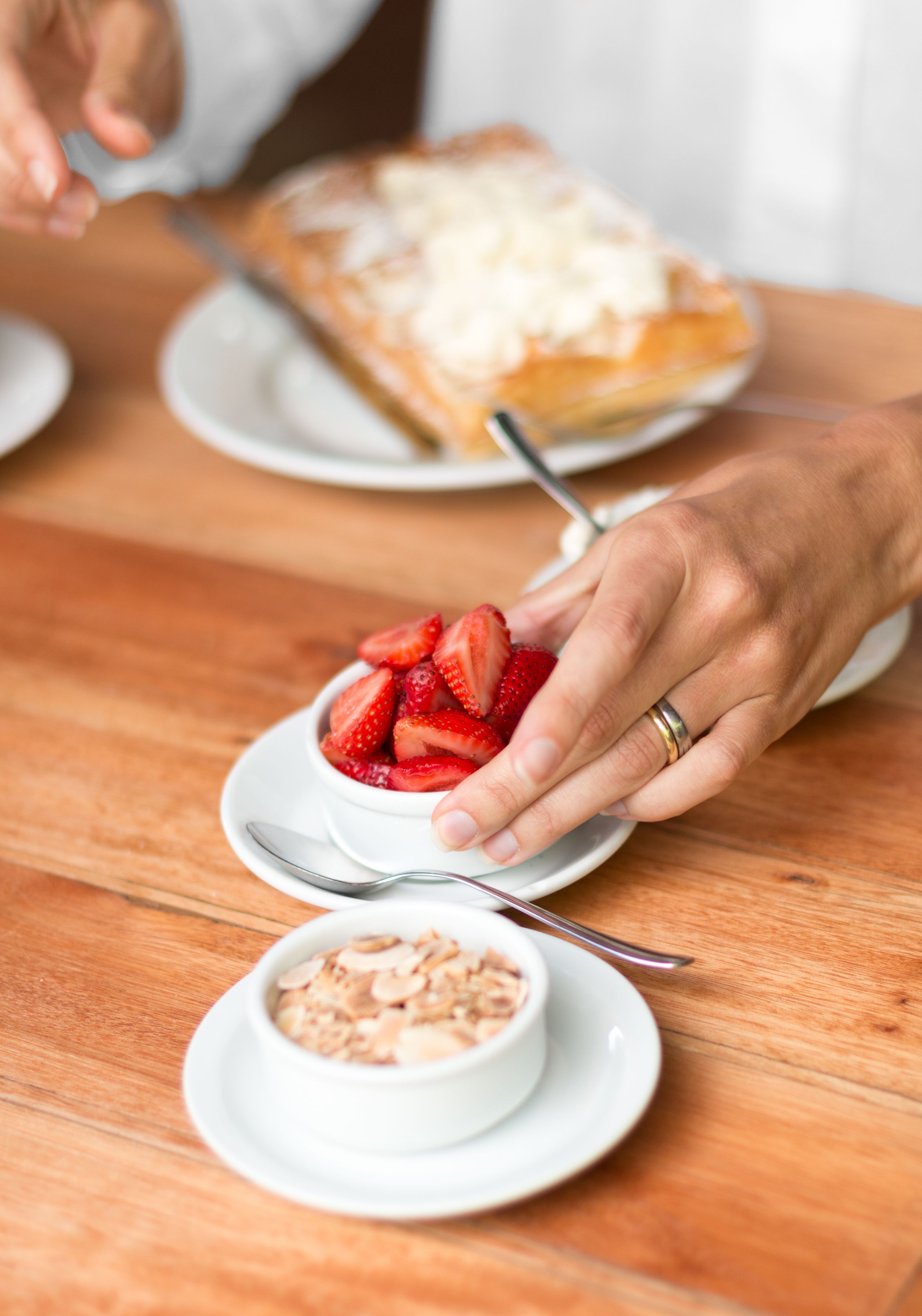Eine Person serviert ein Dessert mit Erdbeeren und einer Kuchenscheibe auf einem Holztisch.