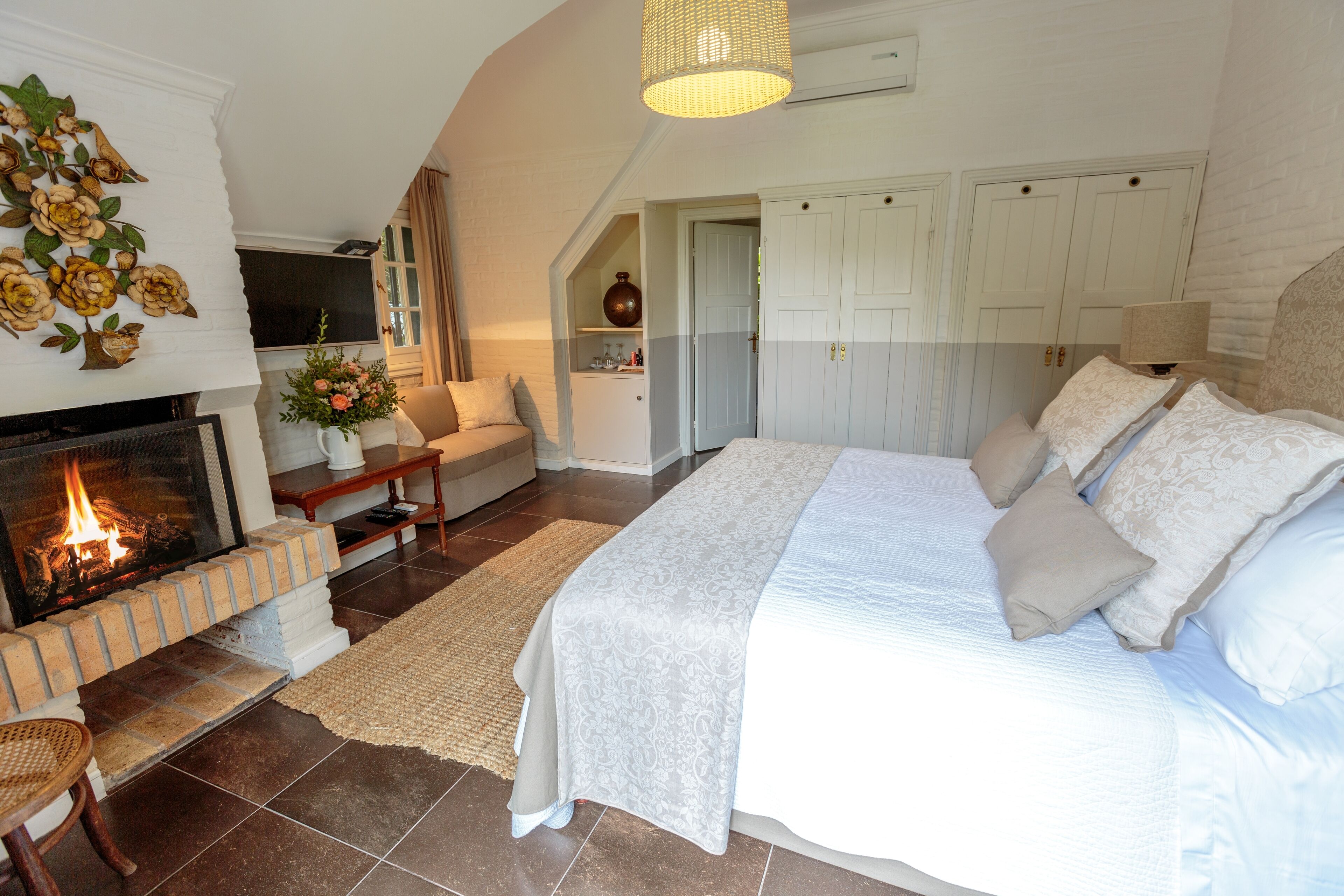 A bedroom with a fireplace, a bed with white linens, a sofa, and a small table with a vase of flowers.