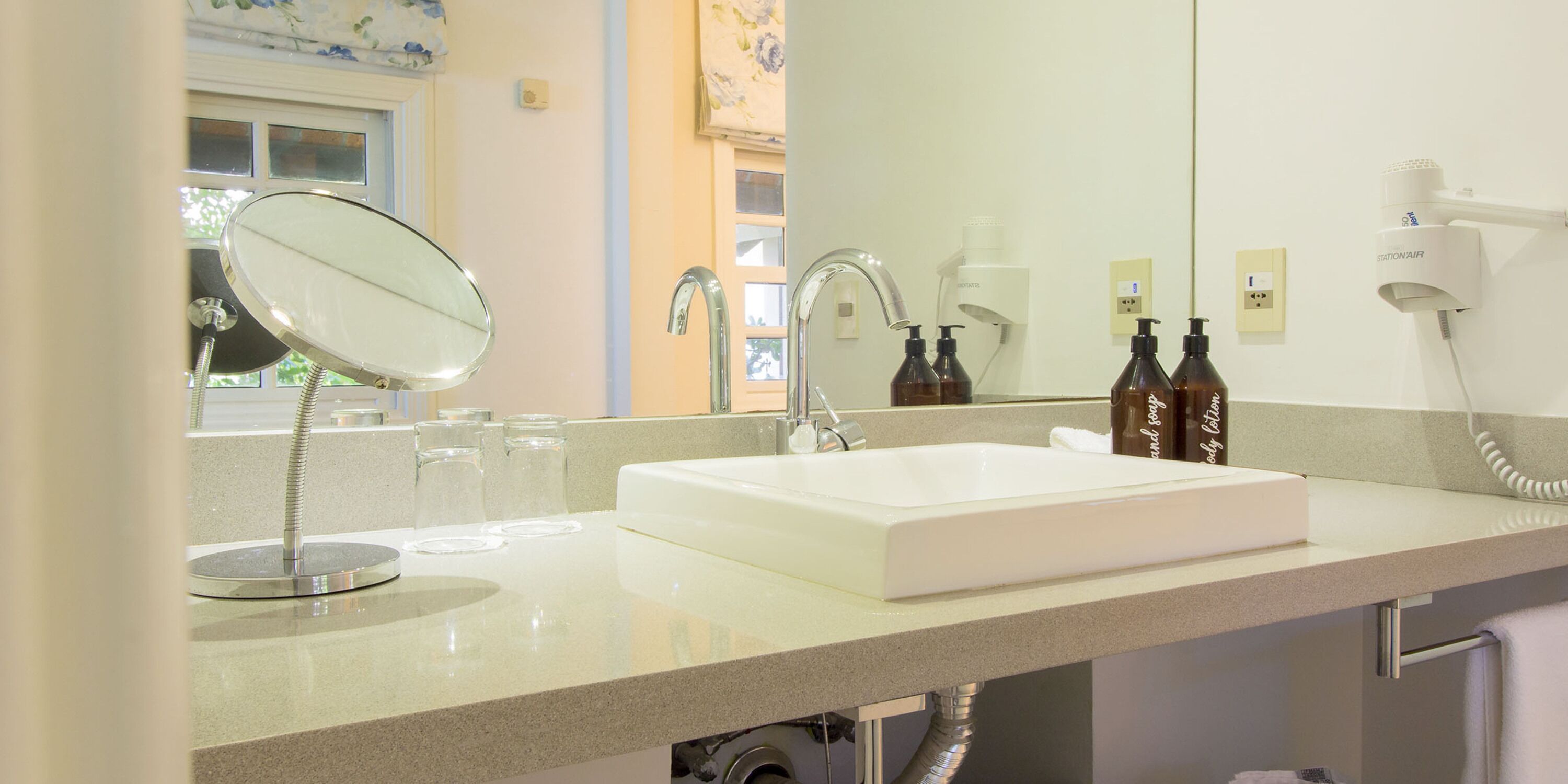 A bathroom with a white sink, a mirror, a handheld showerhead, and a hairdryer mounted on the wall.