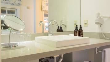 A bathroom with a white sink, a mirror, a handheld showerhead, and a hairdryer mounted on the wall.
