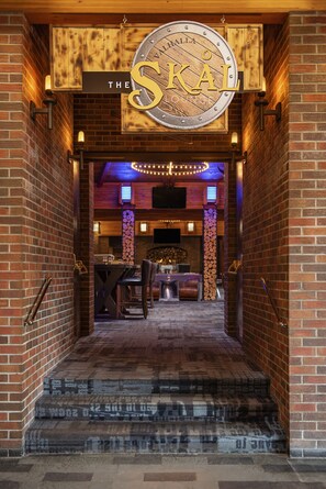 A brick-walled entrance to The Skåle Lounge with a wooden sign above the door, a staircase leading inside, and a seating area visible through the doorway.