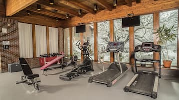Une salle de sport équipée de divers appareils d’exercice, dotée de grandes fenêtres et d’un plafond en bois.