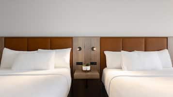 A hotel room with two beds, a wooden headboard, a small table with a plant, and a wall-mounted light fixture.