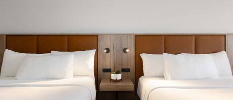 A hotel room with two beds, a wooden headboard, a small table with a plant, and a wall-mounted light fixture.