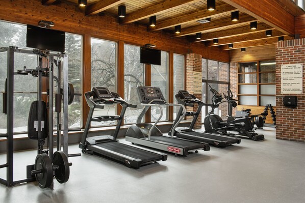 A gym with treadmills, a weight bench, and a TV screen.
