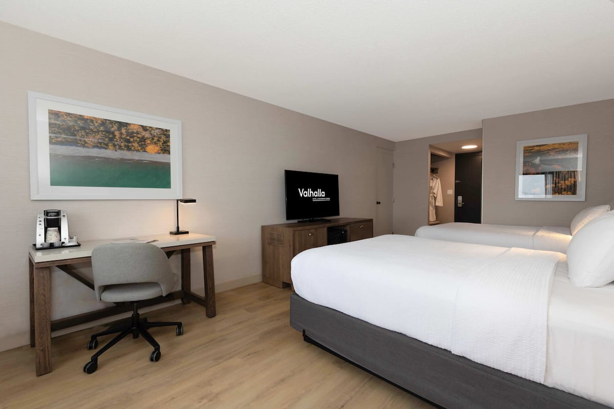 A hotel room with a bed, desk, chair, television, and artwork on the walls.