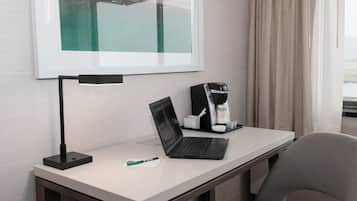 Une chambre d’hôtel équipée d’un bureau, d’un ordinateur portable, d’une machine à café et d’une œuvre d’art encadrée au mur.